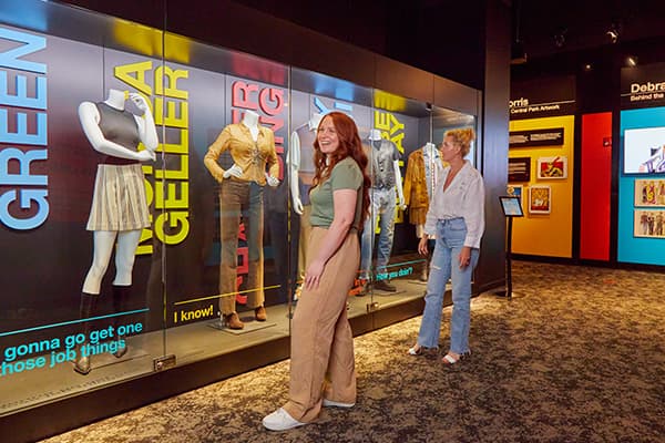 Two women in a museum standing by a display of costumes for Rachel and Monica.