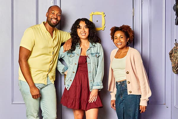 Three people posing in front of the iconic purple apartment door with the yellow peephole frame.