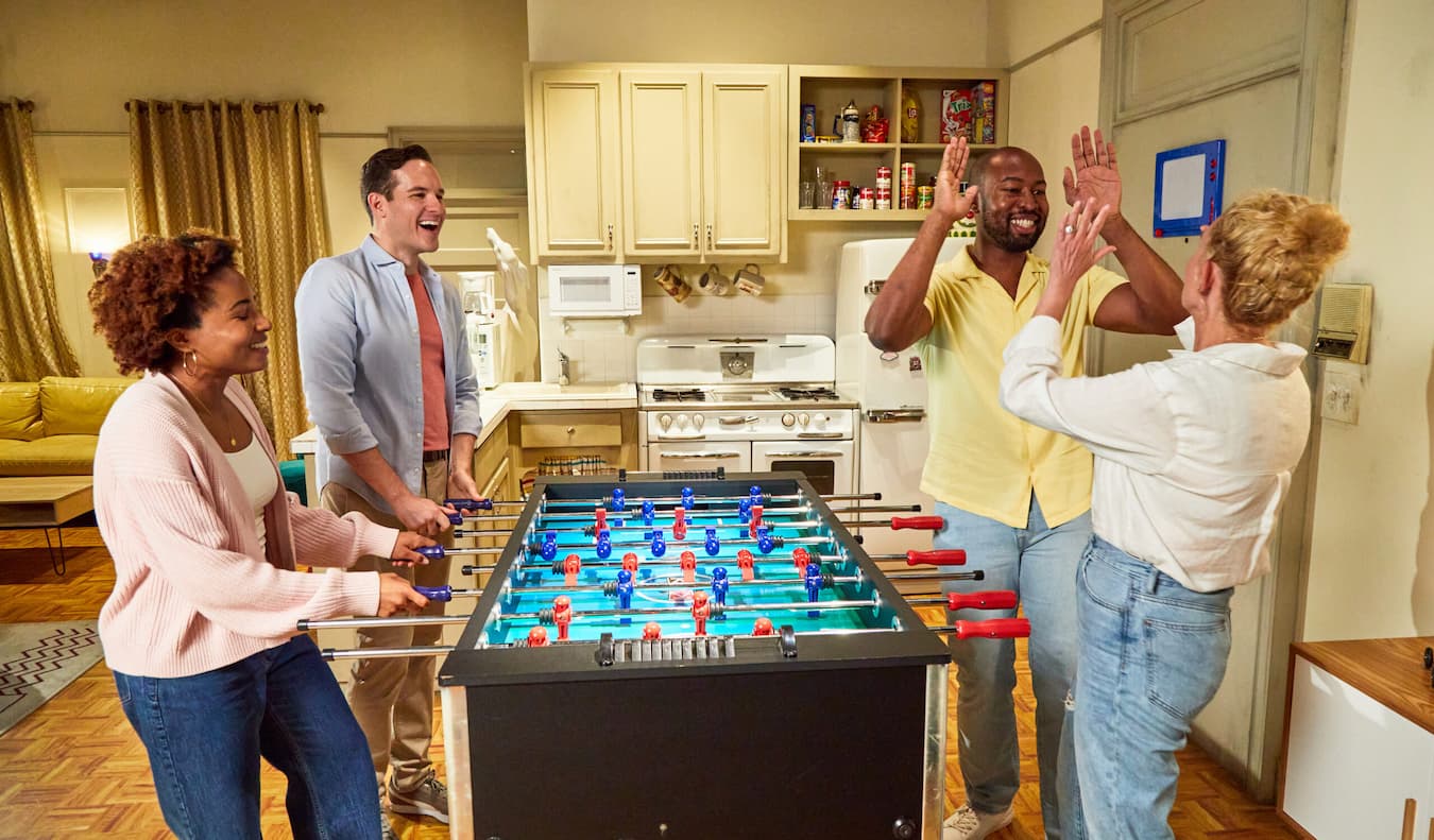 Four friends cheering while playing football in a recreation of the apartment kitchen set.